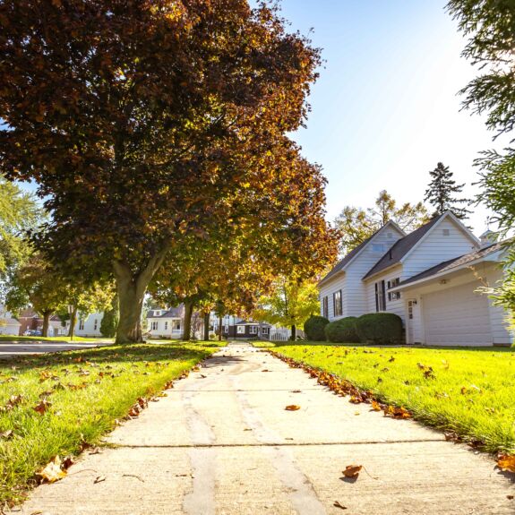 Pelouse résidentielle bien entretenue à l’automne avec des feuilles tombées au sol, illustrant l’entretien de pelouse à l’automne pour préparer le gazon avant l’hiver.